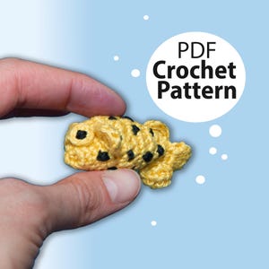 Peut inclure: Un poisson jaune crocheté avec des points noirs. Le poisson est tenu dans une main. Le texte "PDF Crochet Pattern" est dans un cercle blanc sur fond bleu.