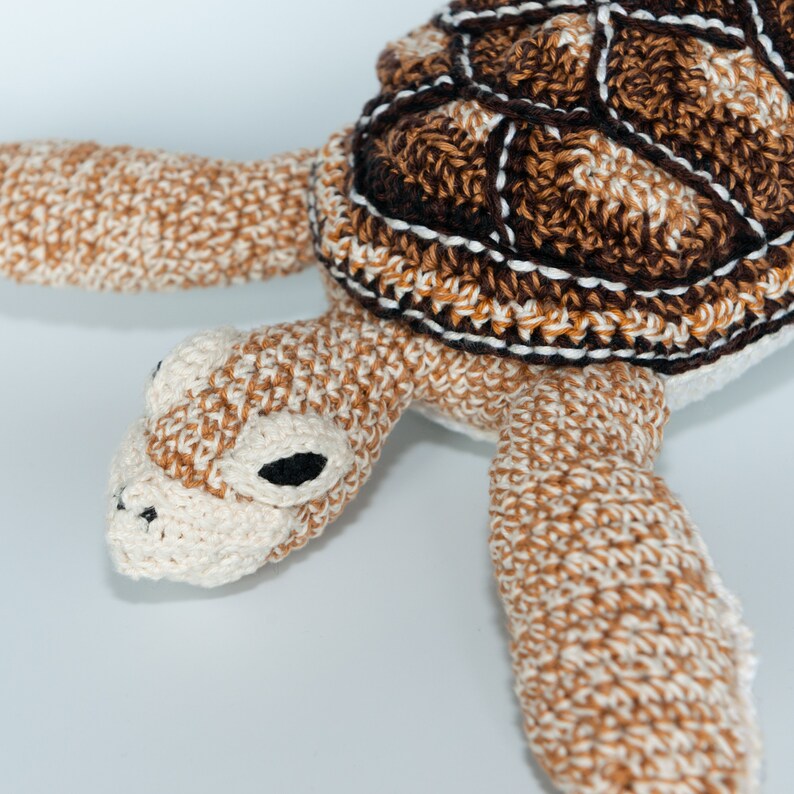 May include: A crocheted turtle toy with a brown and white shell and a white body. The turtle has black eyes and a brown nose.