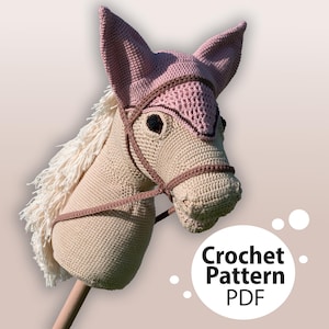 Puede incluir: Patrón de crochet PDF para un caballo de balancín de crochet beige y rosa con una brida de cuero marrón.