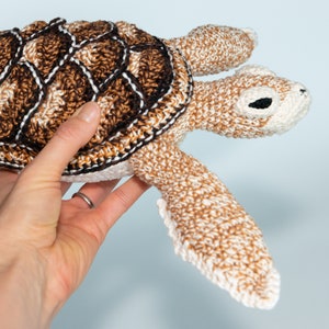May include: A crocheted sea turtle toy with a brown and white shell and a white body. The turtle has black eyes and a brown nose.