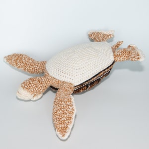 May include: A crocheted turtle toy with a white shell and brown limbs. The turtle is lying on its back with its legs and head outstretched.