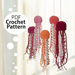 Könnte beinhalten: Eine Sammlung von gehäkelten Quallen in verschiedenen Farben, darunter Rosa, Orange und Burgunderrot, mit weißen und cremefarbenen Tentakeln. Der Text "PDF Crochet Pattern" ist in einem weißen Kreis abgebildet.