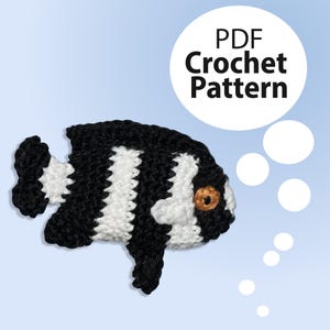 Könnte beinhalten: Ein schwarz-weißer gehäkelter Fisch mit einem orangefarbenen Auge. Der Fisch ist ein Häkelmuster und das Bild enthält den Text "PDF Crochet Pattern".