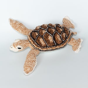 May include: A crocheted sea turtle toy with a brown and white shell and white body. The turtle is lying on its back with its legs and head outstretched.