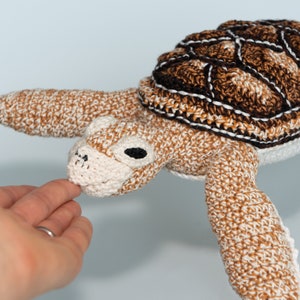 May include: A crocheted sea turtle toy with a brown and white shell and a white face. The turtle is lying on its back with its head and flippers extended.