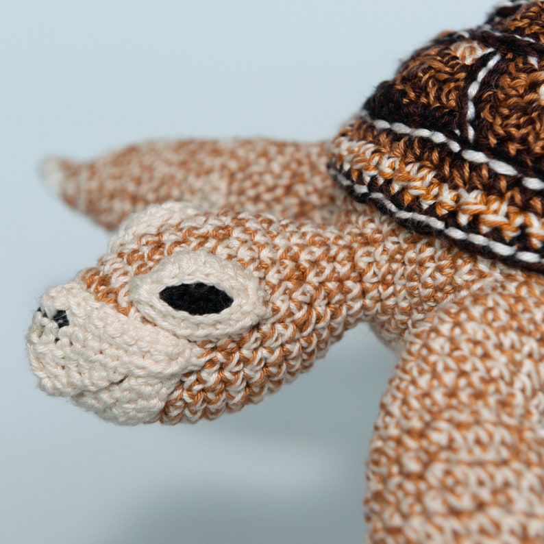 May include: A crocheted turtle toy with a brown and white shell and a beige head with black eyes. The turtle is made with a soft, textured yarn.