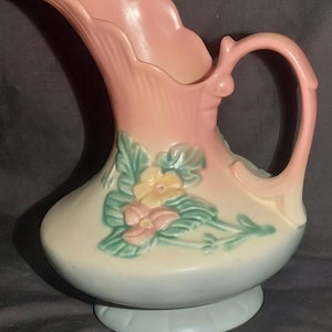 May include: A vintage ceramic pitcher with a pink, white, and blue glaze. The pitcher features a floral design with pink, yellow, and green flowers.