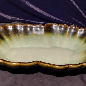 May include: A large, green and brown ceramic serving bowl with a scalloped edge. The bowl is glazed and has a rustic look.