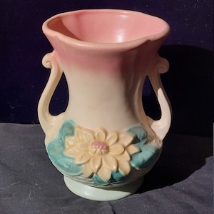Puede incluir: Un jarrón de cerámica vintage con dos asas, que presenta un diseño floral en relieve en tonos amarillos, verdes y rosas.