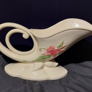 May include: A white ceramic cornucopia vase with a pink and green floral design. The vase has a curled handle and a wide, open top.