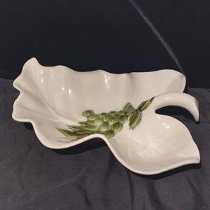 May include: A white ceramic serving dish shaped like a leaf with a green grape design and a handle.
