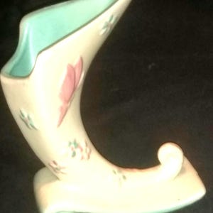 May include: A white ceramic vase shaped like a shoe with a light blue interior. The vase is decorated with pink and green floral designs.