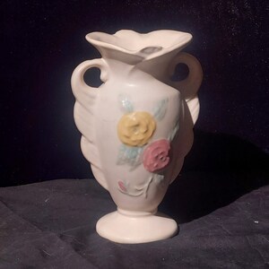 May include: A white ceramic vase with a floral design. The vase has two handles and a ruffled top. The flowers are yellow, pink, and green.