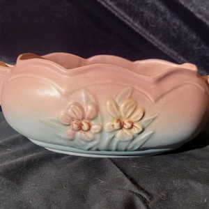 May include: A pink and blue glazed ceramic planter with a scalloped rim and floral design. The planter features two stylized flowers with pink and yellow petals.