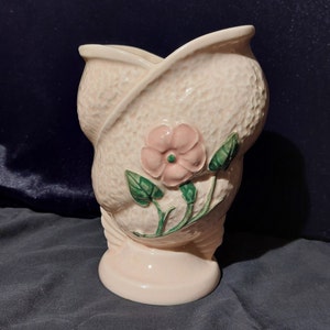 Peut inclure: Un vase en céramique rose avec une surface texturée et un motif floral. Le vase a une large ouverture et une base arrondie.