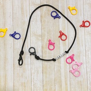 Puede incluir: Un cordón negro con la palabra "FABIAN" en cuentas blancas y varios cierres de plástico de colores. El cordón está hecho de un cordón negro delgado y tiene un diseño simple.