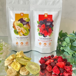 Puede incluir: Dos bolsas de aperitivos de frutas y bayas liofilizadas. La bolsa de la izquierda tiene una imagen de rodajas de piña, kiwi y plátano. La bolsa de la derecha tiene una imagen de fresas, frambuesas y moras. Ambas bolsas tienen el texto "Taste in Nature" y "100% Fruits Mix" o "100% Berries Mix".