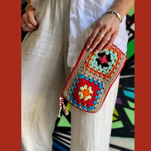 May include: A colorful crocheted clutch bag with a geometric pattern. The bag has a tassel and is made with a variety of colors, including red, orange, yellow, green, blue, and brown.