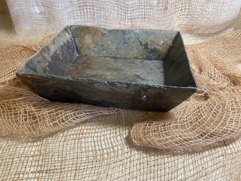 May include: A rectangular slate tray with a rustic, weathered finish. The tray is made of natural slate and has a slightly uneven surface. It is perfect for displaying small items or serving snacks.