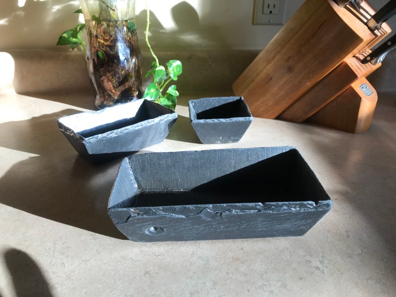 May include: Three black slate rectangular serving dishes of varying sizes. The dishes are made of natural slate and have a rustic, handmade look.