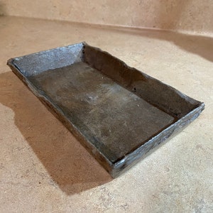 May include: A rectangular metal tray with a rustic, weathered finish. The tray has a slightly raised edge and a smooth, flat interior.