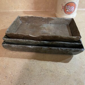 May include: Three stacked slate rectangular trays, each with a slightly different shade of gray. The trays are made of natural stone and have a rustic, organic look.