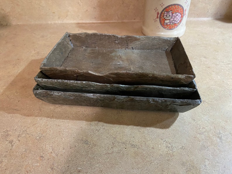 May include: Three stacked slate rectangular trays, each with a slightly different shade of gray. The trays are made of natural stone and have a rustic, organic look.