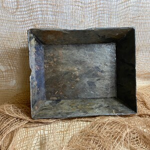 May include: A rectangular tray made of dark gray slate with a rough, textured surface. The tray has a slightly raised rim and is perfect for serving or displaying small items.