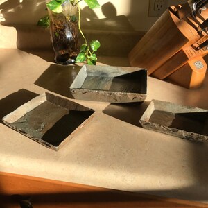 May include: Three rectangular slate trays in various sizes. The trays are made of natural slate and have a rustic, earthy look.