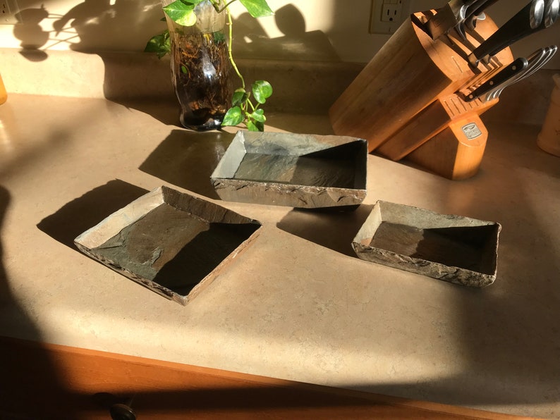 May include: Three rectangular slate trays in various sizes. The trays are made of natural slate and have a rustic, earthy look.