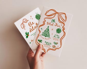Puede incluir: Dos tarjetas de invitación navideñas blancas. Una tarjeta dice "& the details" con acebo y un diseño de lazo. La otra tarjeta dice "Oh What Fun" con un árbol de Navidad, adornos y detalles del evento. Las tarjetas están sujetas por una mano.