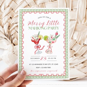 Pode incluir: Um convite branco com uma borda vermelha e verde, com o texto "Merry Little Mahjong Party". S&atilde;o retratados dois copos de coquetel em aquarela, juntamente com a data e hora do evento. O convite &eacute; segurado por uma m&atilde;o.