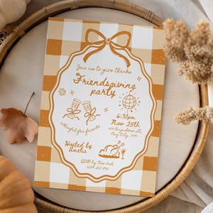 May include: An invitation for a Friendsgiving party with a gingham background. The invitation has a decorative border and includes the text "Join us to give thanks Friendsgiving party" and event details. The invitation is on a wooden tray.