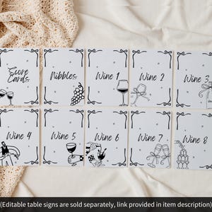 May include: A collection of white table signs with black text and illustrations. The signs include text such as "Score Cards", "Nibbles", and "Wine 1-8". Each sign has a decorative border and a wine-related illustration.