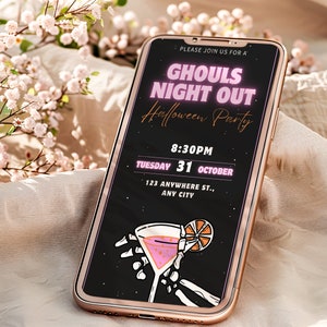 May include: A smartphone screen displaying a Halloween party invitation with the text "Ghouls Night Out Halloween Party" in pink neon lettering. The invitation includes the date, time, and location of the party. A skeleton hand holds a pink cocktail with an orange slice.