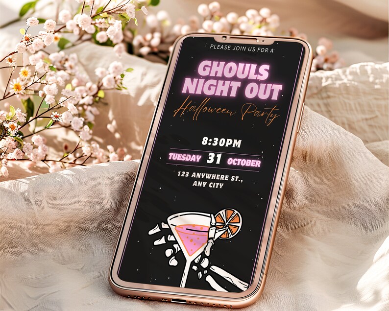 May include: A smartphone screen displaying a Halloween party invitation with the text "Ghouls Night Out Halloween Party" in pink neon lettering. The invitation includes the date, time, and location of the party. A skeleton hand holds a pink cocktail with an orange slice.