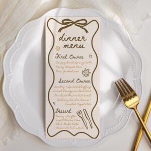 May include: A dinner menu card with a decorative border and bow design, listing courses like Crispy Duck Spring Roll and Benny Trifle. The card is on a white plate with gold cutlery.