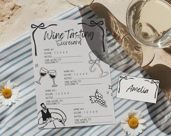 May include: A black and white wine tasting scorecard with the text "Wine Tasting Scorecard". The scorecard includes spaces for wine scores, notes, and a word to describe each wine. A small name card is also present.