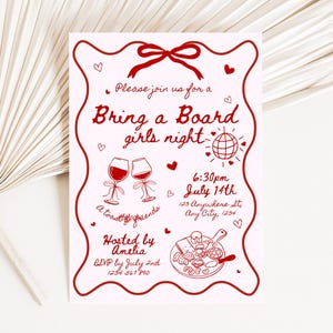 以下が含まれることがあります： 赤色の装飾要素とテキストが入ったピンク色の招待状。「Bring a Board girls night」と書かれており、日付、時間、場所などの詳細が含まれています。装飾要素には、ハート、ワイングラス、地球儀が含まれています。