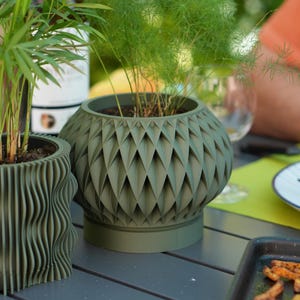 May include: Two green plant pots, one with a diamond pattern and the other with a wavy design. The pots contain soil and plants, creating a natural aesthetic. The larger pot has a diameter of approximately 25 cm.