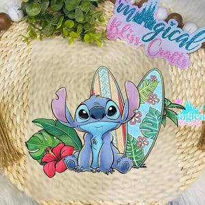May include: A blue Stitch character from Lilo & Stitch is sitting on a surfboard with tropical flowers and leaves. The background is a light brown surface.