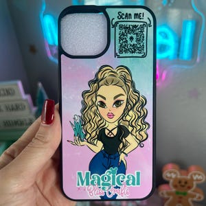 May include: Black phone case with a cartoon illustration of a woman with blonde curly hair, wearing a black top and blue jeans. The case has the text "Magical Bliss Crafts" and a QR code that says "Scan Me!".