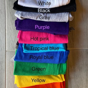Peut inclure: Une pile de t-shirts de diff&eacute;rentes couleurs, dont blanc, noir, gris, violet, rose vif, bleu tropical, bleu royal, vert, jaune, orange et rouge.