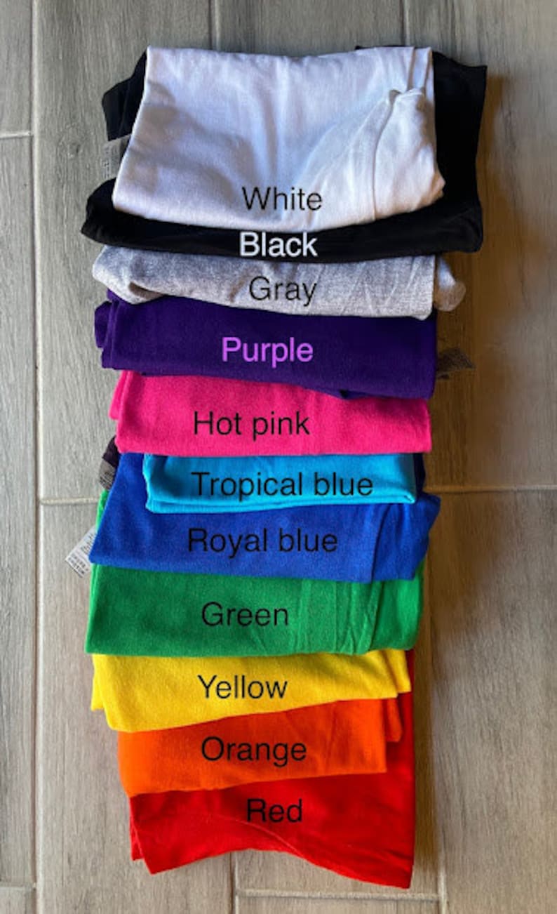 Peut inclure: Une pile de t-shirts de diff&eacute;rentes couleurs, dont blanc, noir, gris, violet, rose vif, bleu tropical, bleu royal, vert, jaune, orange et rouge.
