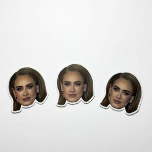 May include: Three die-cut stickers featuring a portrait of a woman with long, light brown hair and dramatic eye makeup. The stickers have a white border and are arranged against a white background.