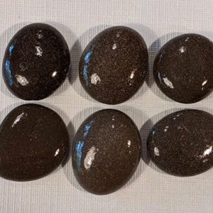 May include: Six smooth, dark brown river rocks, each with a slightly different shape and texture.