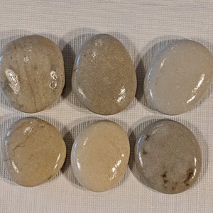 May include: Six smooth, round, natural stones in various shades of brown and beige. The stones are arranged in two rows of three, with the top row slightly offset from the bottom row.