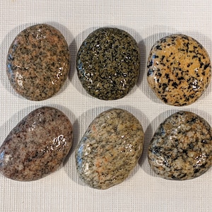 May include: Six smooth, round, polished stones with different patterns of black, brown, and white speckles. The stones are arranged in two rows of three.
