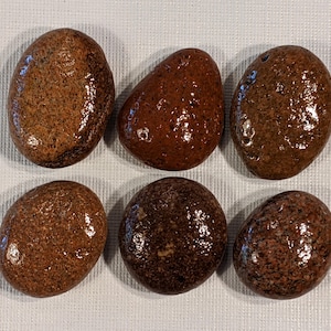 May include: Six smooth, polished stones in various shades of brown and red. The stones are oval-shaped and have a glossy finish.