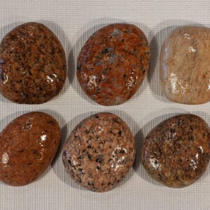 May include: Six smooth, polished river rocks in various shades of brown, pink, and beige. The rocks have a speckled appearance and are arranged in two rows of three.
